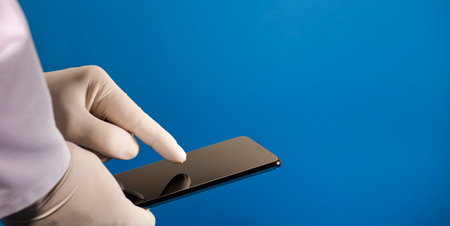 phone in the hands of a doctor (telephone assistance) with surgical glove and blue backgroundの写真素材