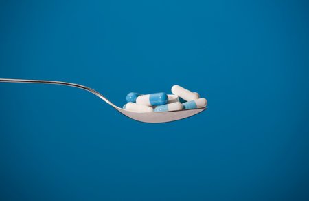 A group of pills on spoon with blue background. Blue and white pills in a spoon. Various...