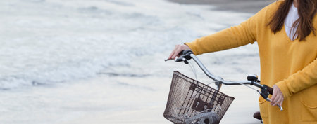 woman with bicycle and yellow sweater, sea with waves in the background, partial view, space for text.の写真素材