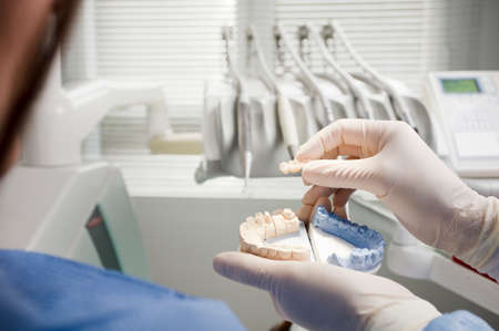 dentist's hand holds mouth bridge, and patient on his back. dental clinic background,