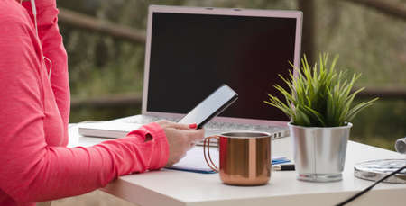 woman with phone in hand, outdoor influencer work table with computer, and office supplies.
