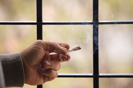 marijuana joint lit, in the hands, with prison gate and forest in the backgroundの写真素材