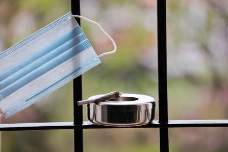 Facial mask with marijuana joint in ashtray with security bars. Social problems, confinement and...