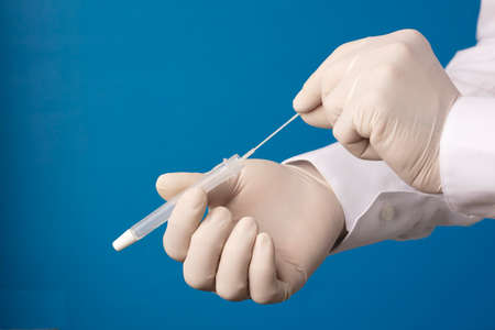 Doctor hands with hyssop and transport vial, process for virus analysis, blue background.の写真素材