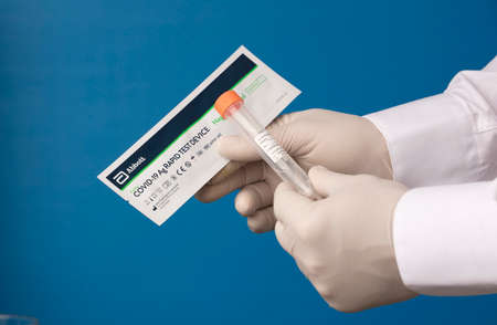 MALAGA, SPAIN- APRIL 8, 2021, doctor's hand with nasal stick for coronary test ABBOTT brand and vial for transport, blue backgroundのeditorial素材