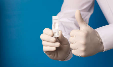 Citizen's hand with rapid test for  virus with negative result and fist with victory gesture, blue background.の写真素材