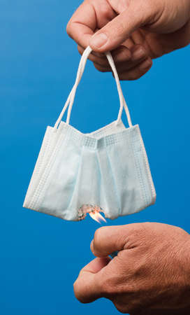 hands burning surgical facial mask, with blue background.の写真素材