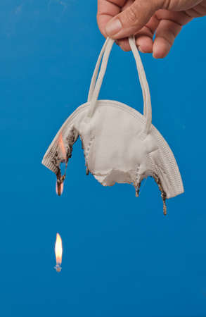 hand with surgical facial mask burning, with blue background.の写真素材