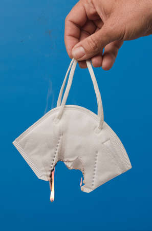 hand with surgical facial mask burning, with blue background.の写真素材