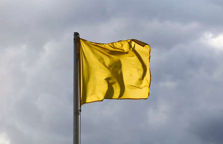 yellow flag flies in the air with clouds rainy dayの写真素材