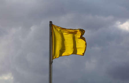 yellow flag flies in the air with clouds rainy dayの写真素材