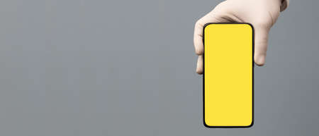 black phone in doctor hand with yellow screen for mockup, gray backgroundの写真素材