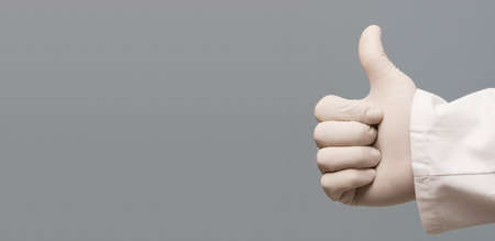 A doctor in blue latex protective glove shows thumbs up as ok sign, isolated on gray backgroundの写真素材