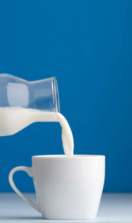 white coffee cup, hand with overturned transparent milk bottle, blue backgroundの写真素材