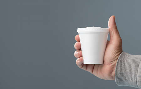 white thermal glass with lid in hand, gray backgroundの写真素材