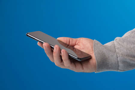 phone in the hands of man with gray sweater, blue background