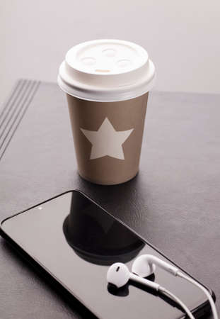 desk with thermal glass of coffee on the table with phone and headphonesの写真素材