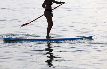 Adventurous girl on a paddle board is paddeling during a bright and vibrant sunsetの写真素材