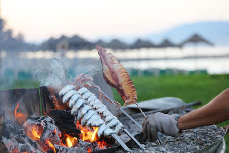 squid in man's hand, fish spit on fire, beach background,