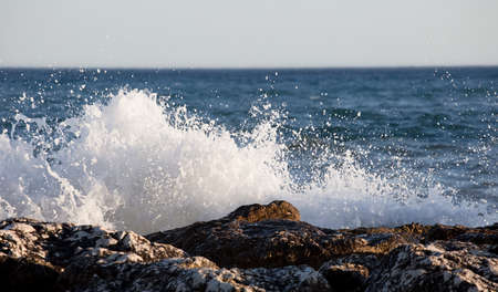 Waves splashed over rocks on a very windy day at sunset (golden hour).の写真素材
