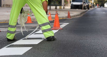 worker in reflective pants removes thermoplastic marking tape from road works to paint traffic lines...