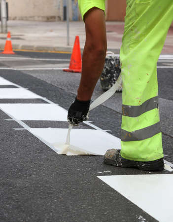 worker in reflective pants removes thermoplastic marking tape from road works to paint traffic lines and bike lanes on asphalt road surface, selective focusの写真素材