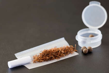 tobacco on cigarette paper, mouthpiece, hash balls and airtight dispenser, dark brown backgroundの写真素材