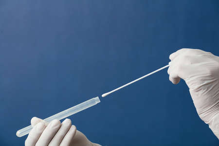 mouth swab in the hands of a doctor or nurse wearing white surgical gloves, inserted into a transporter vial, with a blue backgroundの写真素材