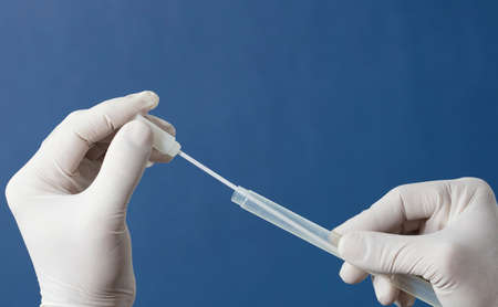 mouth swab in the hands of a doctor or nurse wearing white surgical gloves, inserted into a transporter vial, with a blue backgroundの写真素材