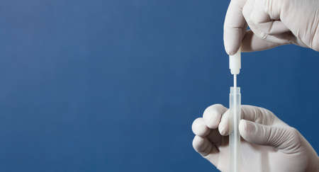 mouth swab in the hands of a doctor or nurse wearing white surgical gloves, inserted into a transporter vial, with a blue backgroundの写真素材