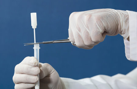 doctor or nurse with scissors and surgical gloves cuts swab, introduces into transparent vial, blue backgroundの写真素材