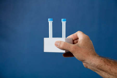 patient hands with medium transport tube kit for pcr analysis, in cardboard holder, blue backgroundの写真素材