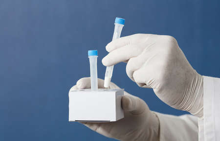 pcr kit in the hands of a doctor with surgical gloves, places medium transport tubes in cardboard support, blue backgroundの写真素材