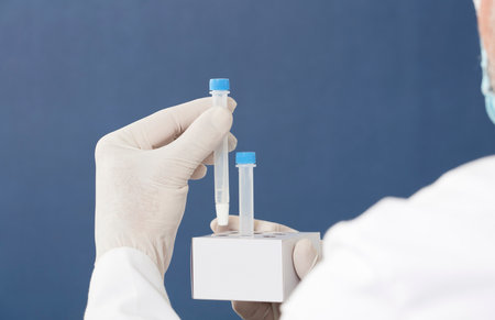 pcr kit in the hands of a doctor with surgical gloves, places medium transport tubes in cardboard support, blue backgroundの写真素材