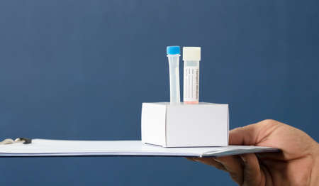 nurse's hands with surgical gloves, medium transport tubes for pcr analysis, in cardboard holder, with data folder, blue backgroundの写真素材