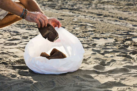 Clean the beach from trash. Man hand picking up empty trash from soda cans from the beachの写真素材