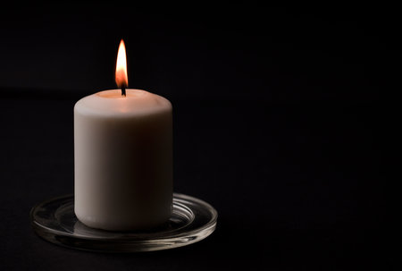 burning candle with flame, man's hands lighting candle, black background. (focus on candle)の写真素材