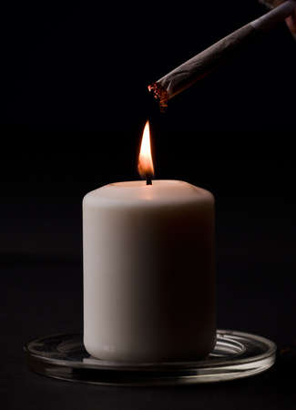 burning candle, with cigar with fire black background. (focus on candle)の写真素材