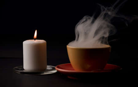 cup of tea with hot smoke and lit candle. on the desk at home, power outage (focus on lit candle)の写真素材