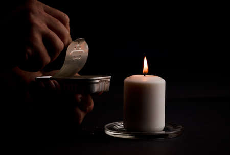 concept of energy blackout, lit candle, with can of preserves in man's hands, energy poverty. (focus on candle)の写真素材