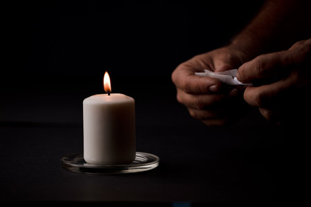 candle lit with flame, man's hands holding a cigar, black background. (focus on candle).の写真素材
