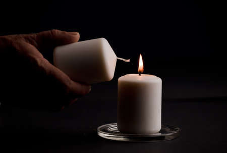 burning candle with flame, man's hands lighting candle, black background. (focus on candle).の写真素材