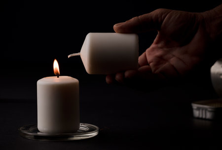 burning candle with flame, man's hands lighting candle, black background. (focus on candle).の写真素材