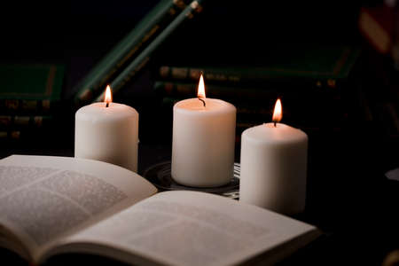 candles with flame, and reading book on desk, black background. (focus on candle).の写真素材