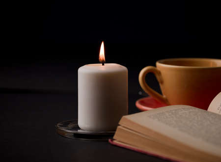 home study table with candles with flame and reading book, (focus on candle).の写真素材