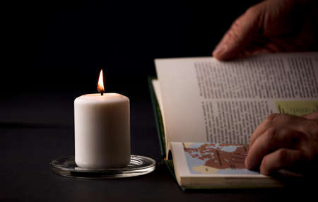 table at home with candles with flame and reading book in hands, (focus on candle).の写真素材