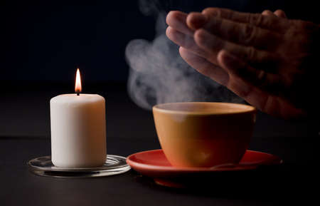 candle with flame, with yellow cup and smoke, hands warming with the heat of the drink, (focus on candle)の写真素材