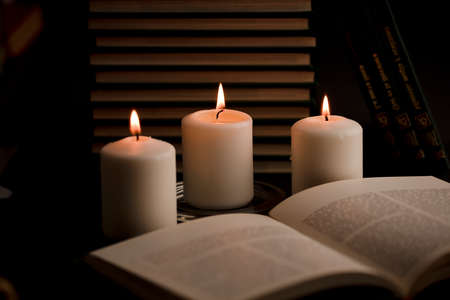 home study table with candles with flame and reading book, (focus on candle)の写真素材