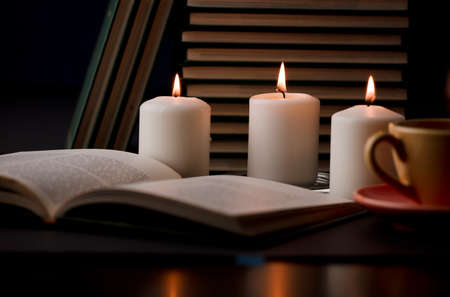 study table with candles with flame and reading book and partial view of cup, (focus on candle).の写真素材