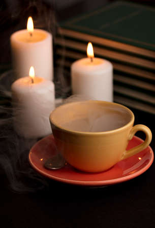 cup of coffee with smoke and candles alfon with books (focus on cup).の写真素材